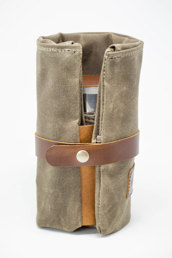 Brown suede roll-up traveling cocktail kit with leather strap and button closure.